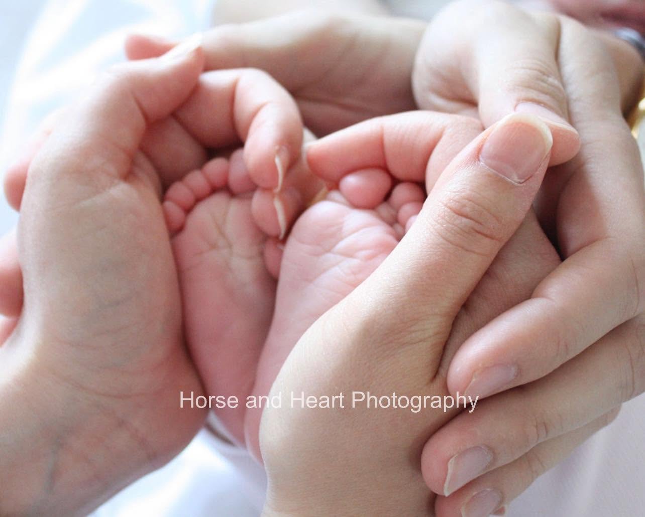 A newborn baby's feet cradled in their parents' hands