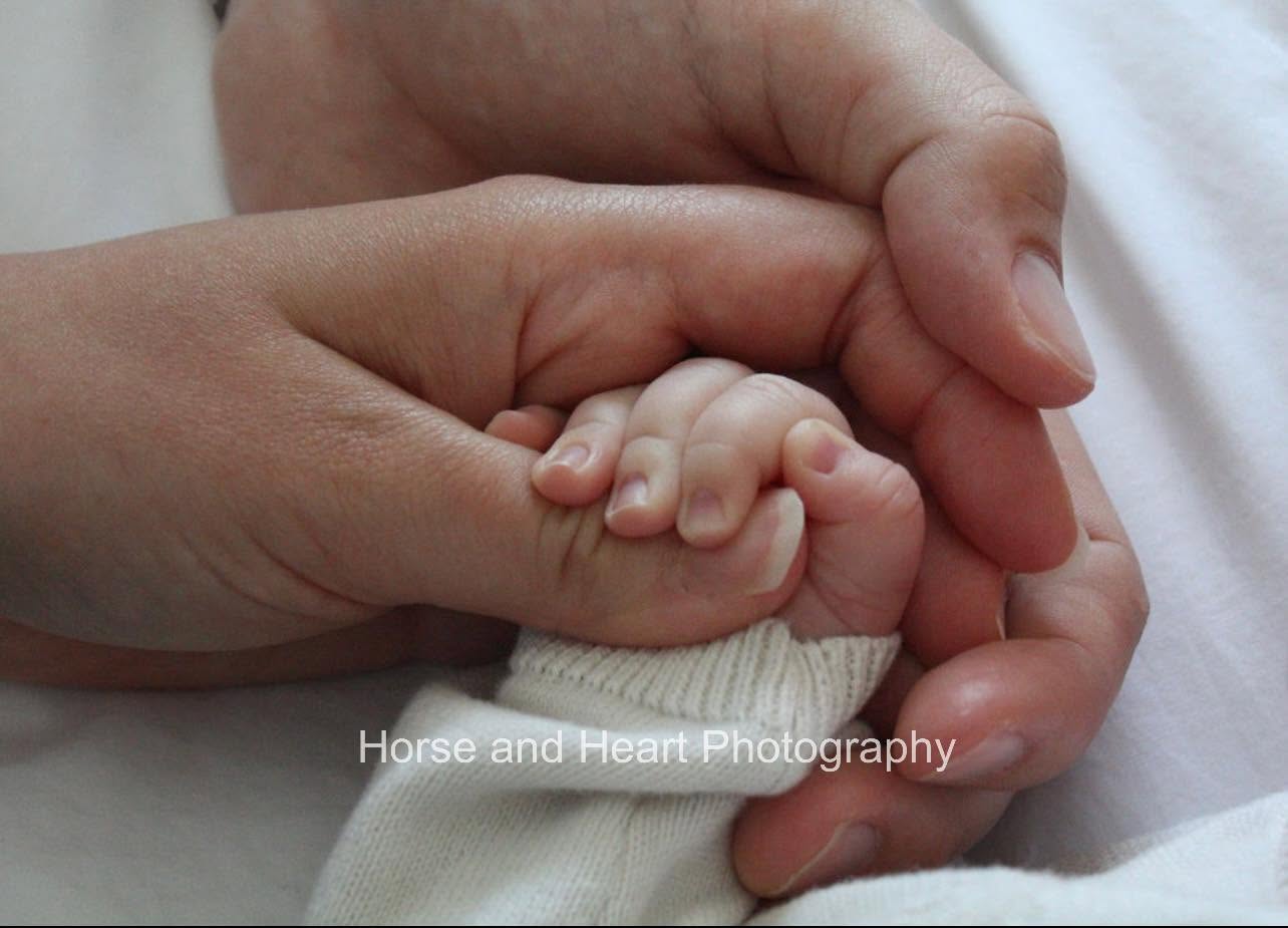 A newborn baby's tiny hand wrapped around a parent's finger